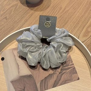 Eleganter silberner Haargummi mit Goldglitzer und handgefertigtem Etikett auf Tablett