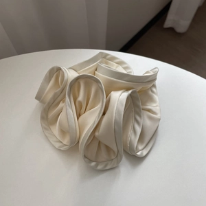 Detailed view of large cream satin scrunchie with ruffled edges on a white table