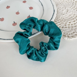 Elegant dark green satin scrunchie with silky finish on a decorative lace background