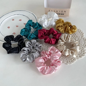 Flat lay of eight colorful satin silk scrunchies on a white background with decorative props