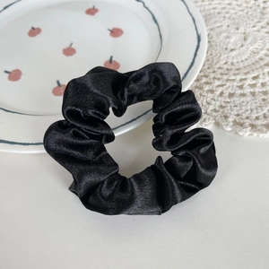 Elegant black satin scrunchie with high glossy texture on a white decorative background plate