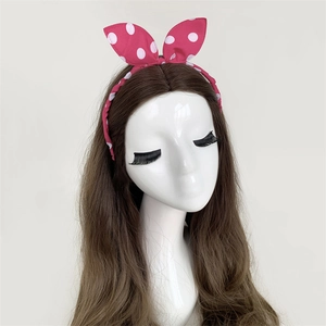 Pink polka dot headband with rabbit ear bow detail shown on a model head stand