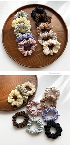 Detail shot of assorted silk satin scrunchies in 10 soft colors on a wooden tray