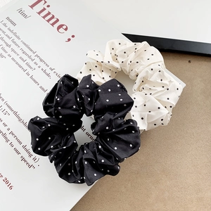 Pair of elegant satin polka dot scrunchies in black and white on a minimalist magazine