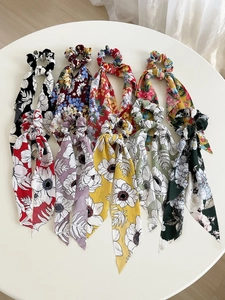 Flat lay of nine colorful floral printed chiffon hair scrunchies with long ribbons on white table