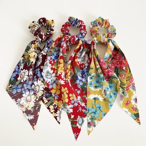 Three floral print scrunchies with long ribbons in burgundy, red, and yellow floral patterns