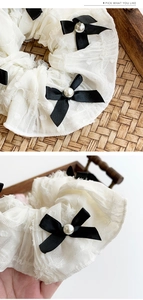 Detailed view of white polka dot lace scrunchie with black bows and pearl accents