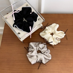 Three elegant satin scrunchies in black, cream, and grey with delicate bow details