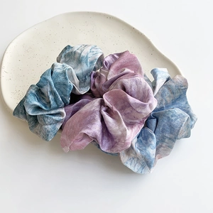 Tie-dye satin scrunchie with pastel watercolor print on a white ceramic tray