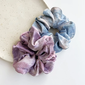 Two-piece tie-dye satin hair scrunchies in blue and purple marble patterns on ceramic tray