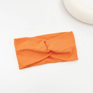 Detail of orange ribbed knit yoga headband showing center cross knot design and fabric texture