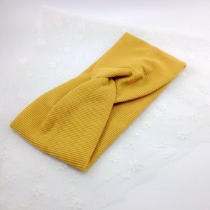 Detail view of ginger yellow ribbed knit headband with cross knot design on lace background