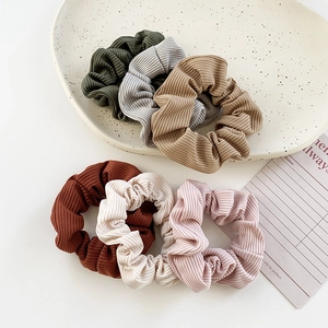 Set of six ribbed velvet hair scrunchies in earthy tones on a minimalist white display