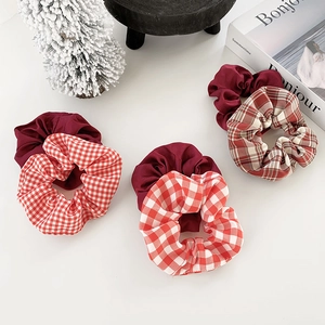 Three elegant red plaid and solid color scrunchies arranged with holiday decor