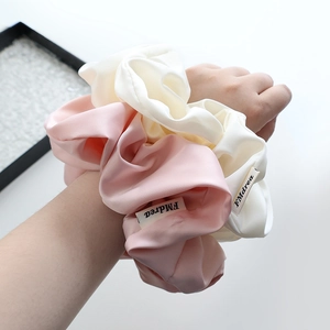 Chouchous géants en satin de soie rose et crème portés au poignet pour un style chic