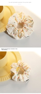 Detail eines cremefarbenen Scrunchies mit Erdbeerdruck und gewebtem Markenetikett