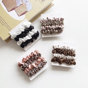 Three-piece satin scrunchie set in assorted neutral colors on a white display card