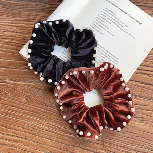 Elegant velvet hair scrunchies with white pearls in black and caramel on a wooden surface