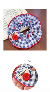 Detailed view of blue plaid scrunchie with cherry patterns, red piping and button accents