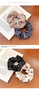 Detail of four flocked bow print scrunchies in beige and grey on a vintage book