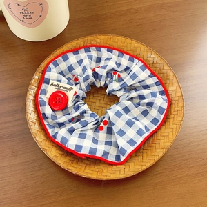 Blue plaid scrunchie with red cherry print and decorative button in a bamboo tray