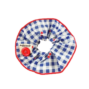 Blue plaid scrunchie with cherry print, red button detail, and woven label on white background