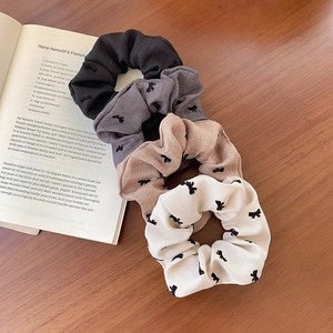 Set of four bow print scrunchies in black, grey, khaki, and cream on a wooden table