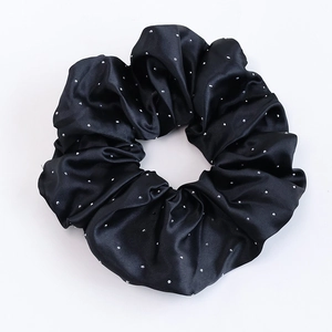 Détail d'un chouchou en satin noir avec strass argentés et texture plissée élégante