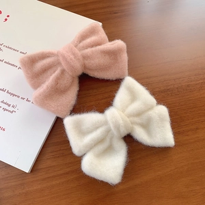 Plüsch-Haarspangen mit Schleifen in Rosa und Cremeweiß auf einem Holzschreibtisch