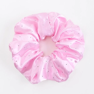 Détail d'un chouchou en satin rose avec strass argentés et texture plissée soyeuse élégante