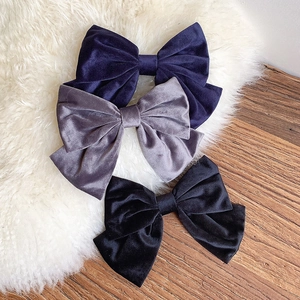 Three large velvet bow hair clips in navy, grey, and black on a soft plush and wood surface