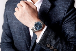 Gros plan d'une montre homme avec cadran bleu et bracelet acier sur une manche de costume