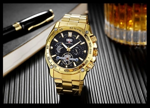 Luxurious gold stainless steel watch displayed with a business pen and a glass of whiskey