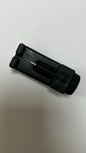 Detail view of the manual black watch band link remover tool with metal pin on white base