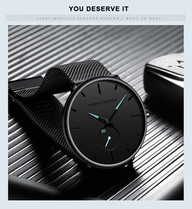 Detailed close-up of a matte black quartz watch with cyan hands and a woven metal mesh strap