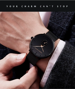 Macro shot of a black stainless steel mesh watch with rose gold dial details and suit sleeve