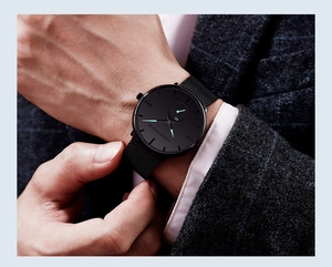 Close-up of minimalist black men's watch with steel mesh strap on a blue suit sleeve