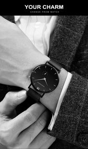 Detail of minimalist watch featuring a black dial with silver hands on a woven mesh strap