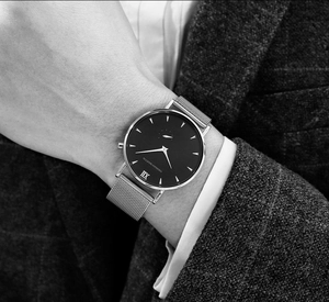Detailed close-up of a silver mesh strap watch and black dial against a business suit