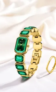 Dettaglio di orologio di lusso oro con cristalli verdi su sfondo di seta bianca