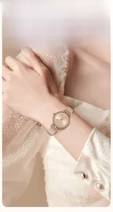 Close-up of rose gold mesh watch with sunray dial and gemstone markers on a woman's wrist