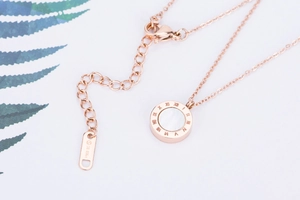 Gros plan d'un collier en or rose avec pendentif romain et chaîne de réglage à l'extrémité
