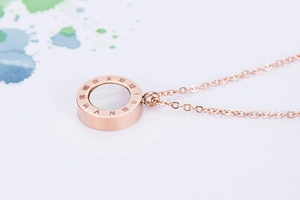 Détail du collier en or rose avec pendentif anneau aux chiffres romains et nacre blanche
