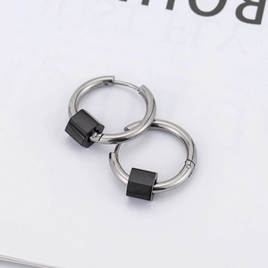 Boucles d'oreilles créoles argentées avec pendentifs cubes noirs sur fond de magazine blanc