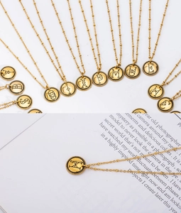 Detailansicht der 18K vergoldeten Münzhalskette mit Buchstaben auf kunstvollem Papier