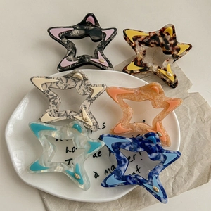 Star-shaped acetate claw hair clips in six different colors on a white ceramic plate