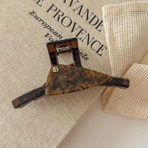 Detail of tortoise shell acetate hair claw clip featuring a golden letter B metal logo