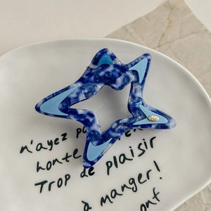 Macro shot of blue marble pattern acetate star hair claw clip on white ceramic plate