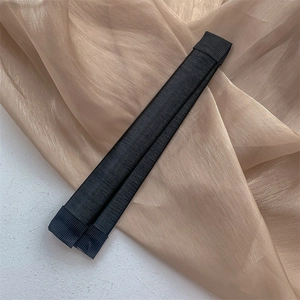 Détail de l'accessoire chignon en tissu noir sur fond de gaze couleur champagne