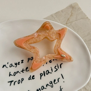 Detail view of large hollow star hair claw in orange marble acrylic on a ceramic plate